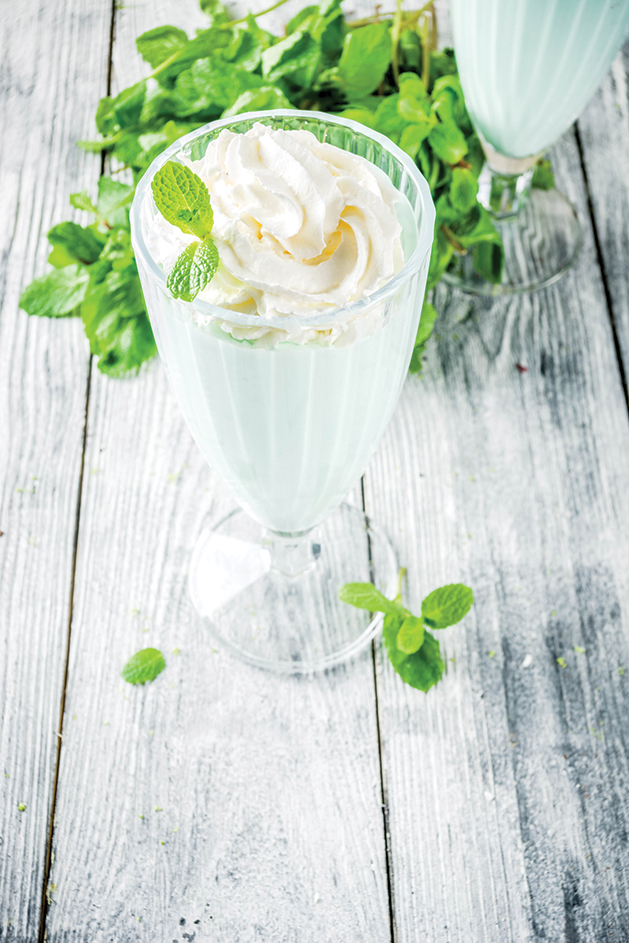 Summer refreshing cocktail, shamrock mint shake, sweet milk drink with fresh mint leaves, wooden background copy space