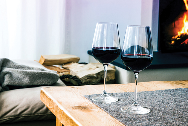 close-up of two glasses with red wine on table in living room with fireplace in the background