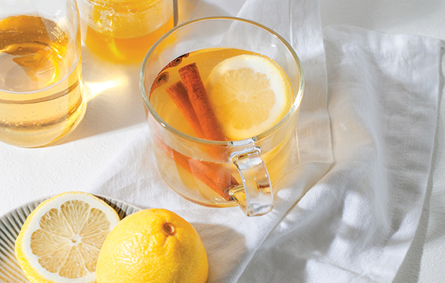 Hot Toddy cocktail drinks with lemon, honey and cinnamon stick in glass on white background. Spiced winter drink