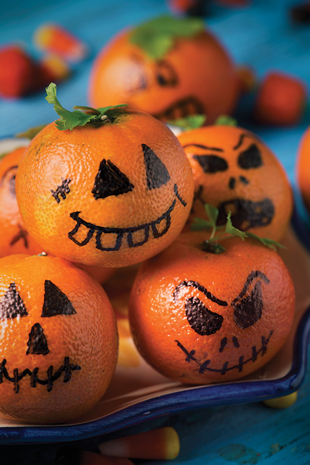 closeup of some tangerines ornamented as carved pumpkins with funny faces on a table sprinkled with different halloween candies