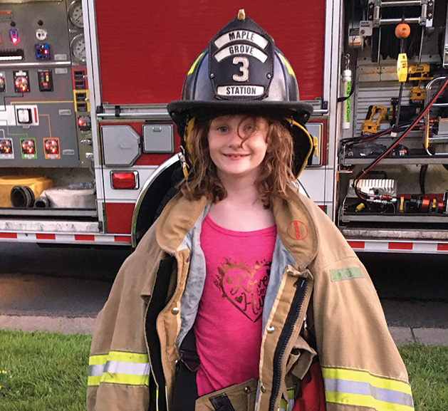 A girl at National Night Out in Maple Grove wears equipment from the Maple Grove Fire Department