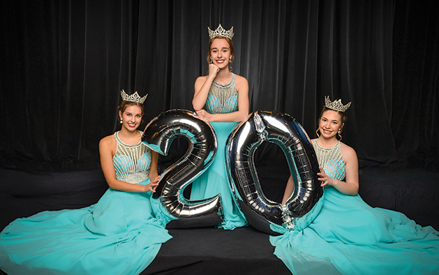 Three Maple Grove ambassadors in blue dresses hold a silver "20" balloon.
