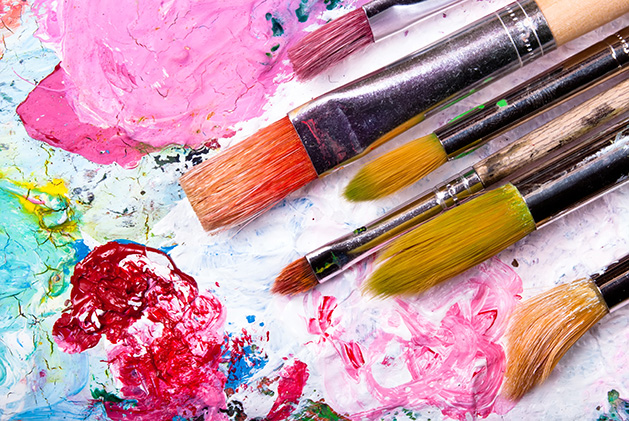 A set of paintbrushes sits on a colorful palate.