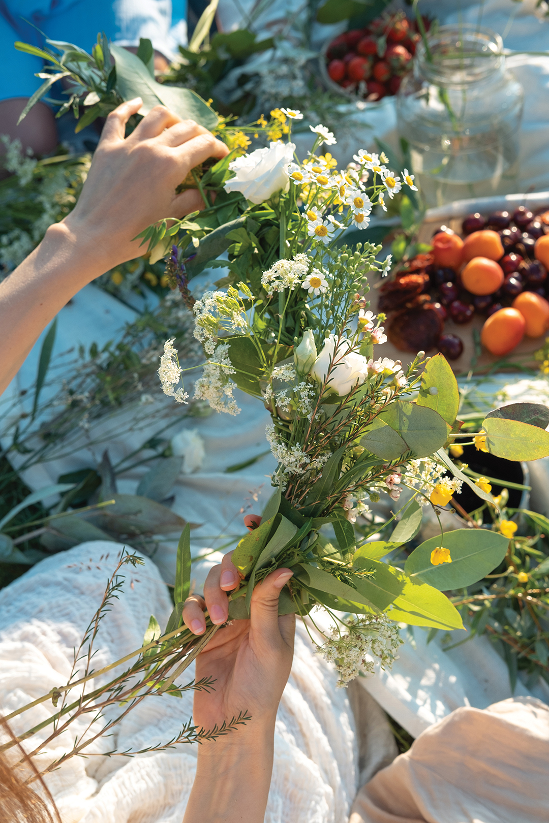 Unrecognized woman weaves a wreath of wild flowers for the summer solstice at master class. Vertical life style photo.