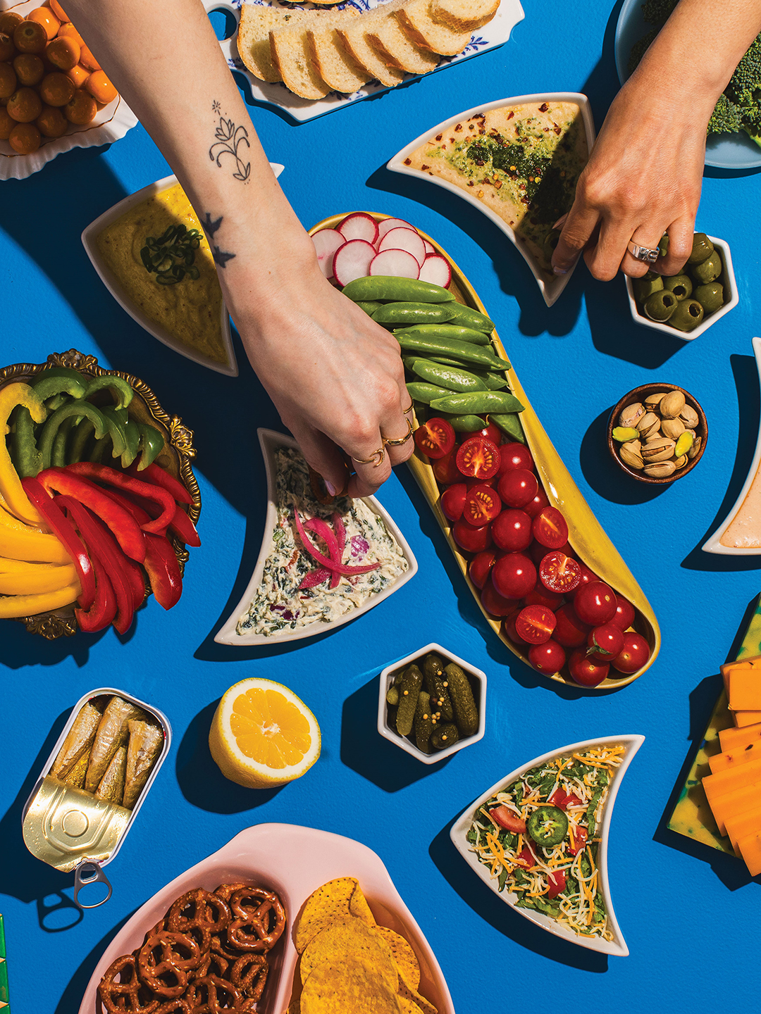 Two hands dipping chips into bowls of dip.